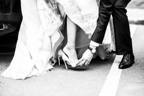 groom helps bride with her shoes