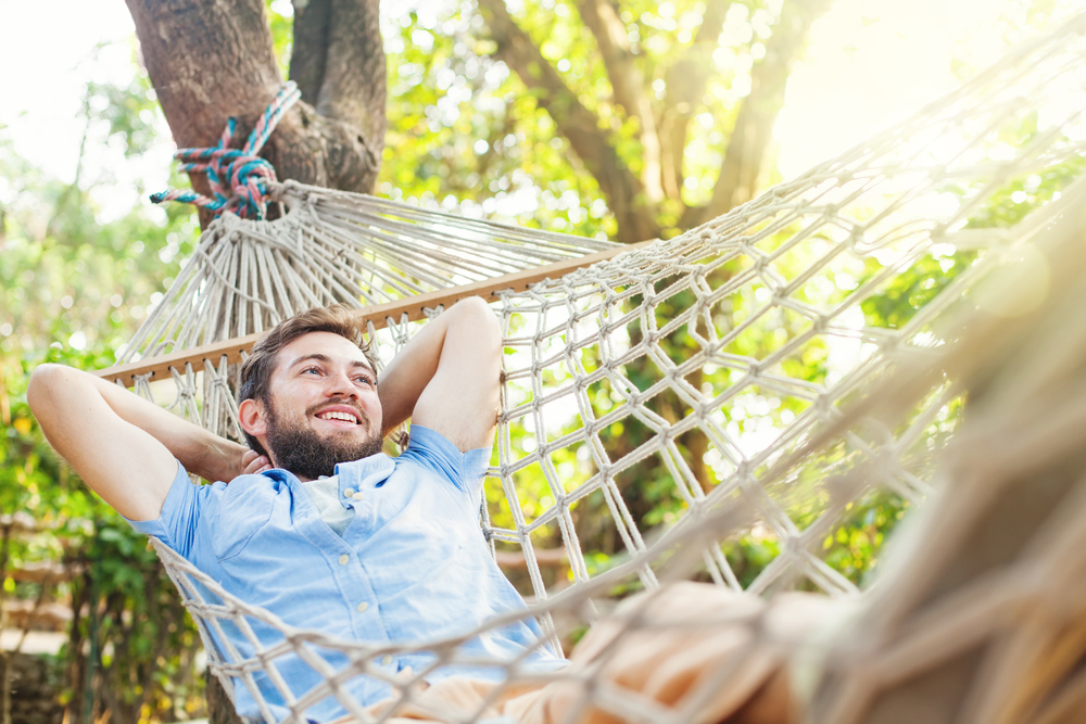 smiling man swinging in a hammock outdoors